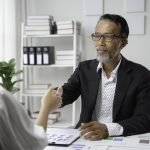 senior manager and young female professional shaking hands in a bright office during a business meeting